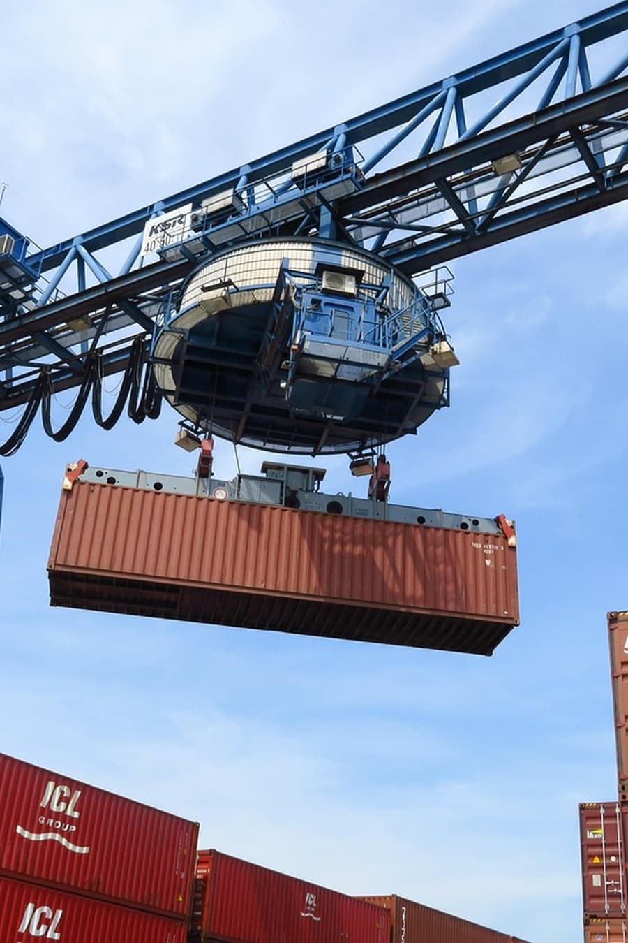 Ship-to-shore gantry crane lowering a shipping container over stacked boxes at a port — container handling and freight forwarding training